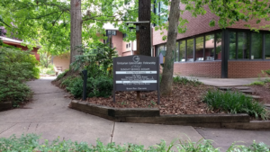 The lower courtyard area outside of the UUFR building. A Pathway of concrete and a leaf strewn landscaped bed where a large sign for the Unitarian Church sits.